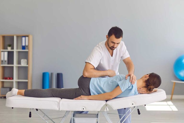 A chiropractor using a stainless steel instrument to treat a patient's forearm in a clinic setting.