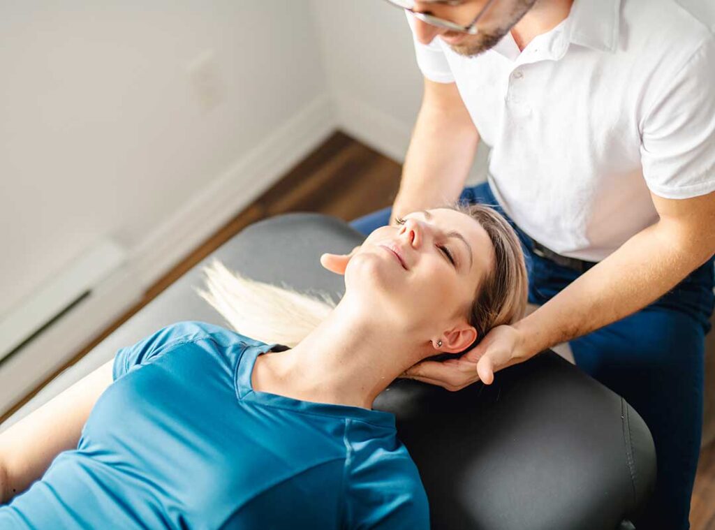 A chiropractor gently adjusting a patient's upper back in a bright, clinical office setting.